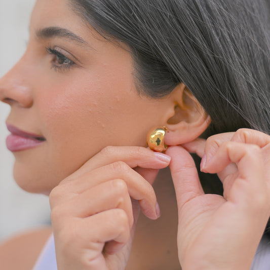Mujer poniendose argollas de acero inoxidable doradas medianas